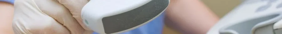 Dettaglio in primo piano della mano di un fisioterapista con guanto che mostra la testina (trasduttore) del dispositivo per ultrasuoni.