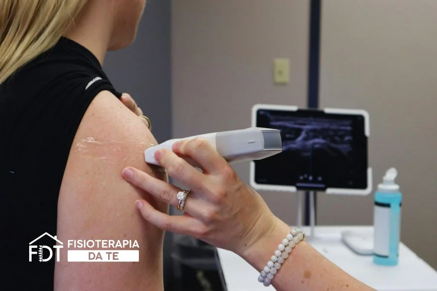 Fisioterapista applica la testina degli ultrasuoni sulla spalla di una paziente utilizzando gel conduttore e monitorando i parametri su tablet.